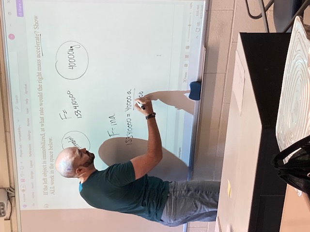 Instructor writing on a whiteboard with class materials projected onto it