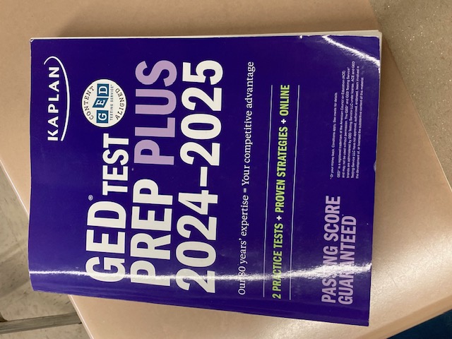 Kaplan GED Test Prep Plus 2024-2025 textbook on a desk